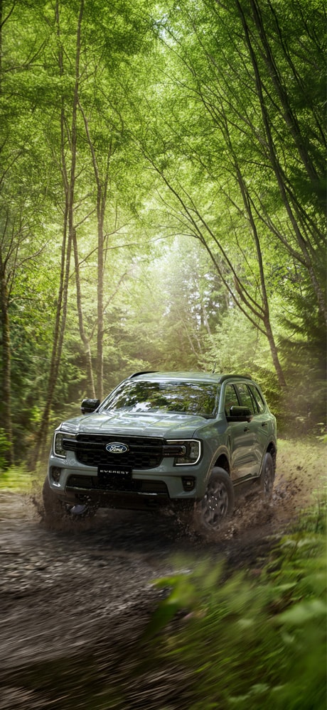 Ford Everest Sport azul en vista frontal de tres cuartos sobre un campo, con montañas al fondo.