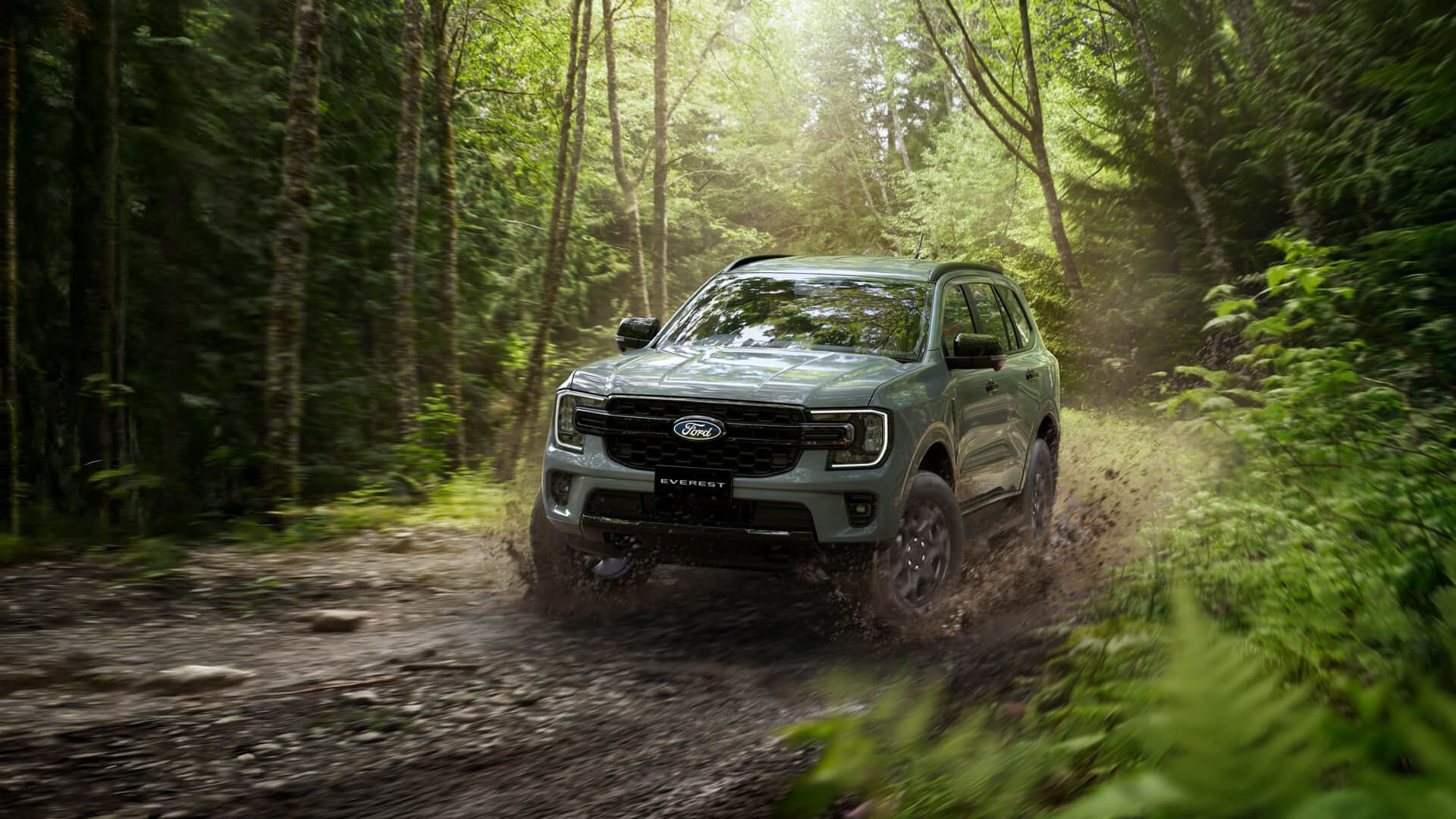 Ford Everest Sport azul en vista frontal de tres cuartos sobre un campo, con montañas al fondo.