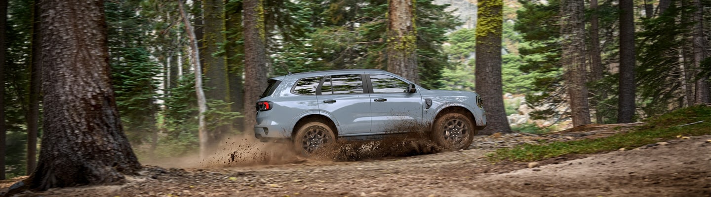 Ford Everest Sport gris en vista lateral mientras recorre un camino con lodo en un bosque.