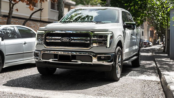 Ford F-150 blanca en vista frontal de tres cuartos sobre una avenida arbolada.