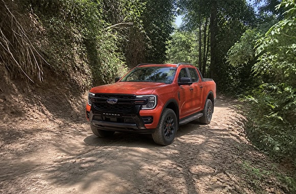 Ford Ranger naranja en vista frontal de tres cuartos sobre un camino de tierra rodeado de vegetación.