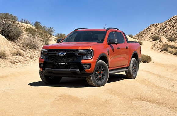 Ford Ranger naranja en vista frontal de tres cuartos sobre un camino de tierra en un entorno rocoso.