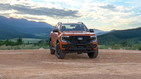 Ford Ranger Wildtrack naranja en vista frontal sobre un camino de tierra, con montañas al fondo.