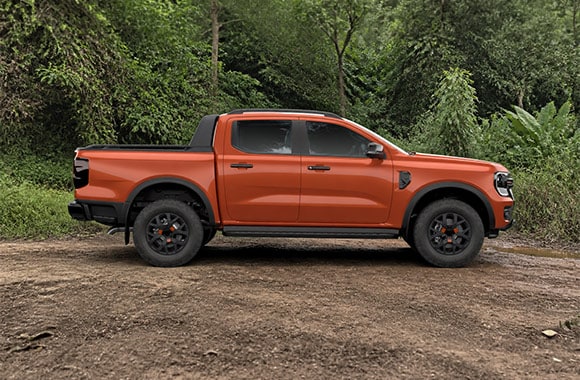 Ford Ranger naranja en vista lateral sobre un camino de tierra rodeado de vegetación.