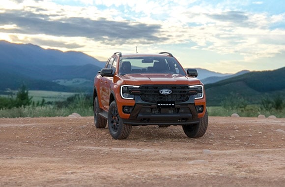 Ford Ranger naranja en vista frontal sobre un camino de tierra, con montañas al fondo.